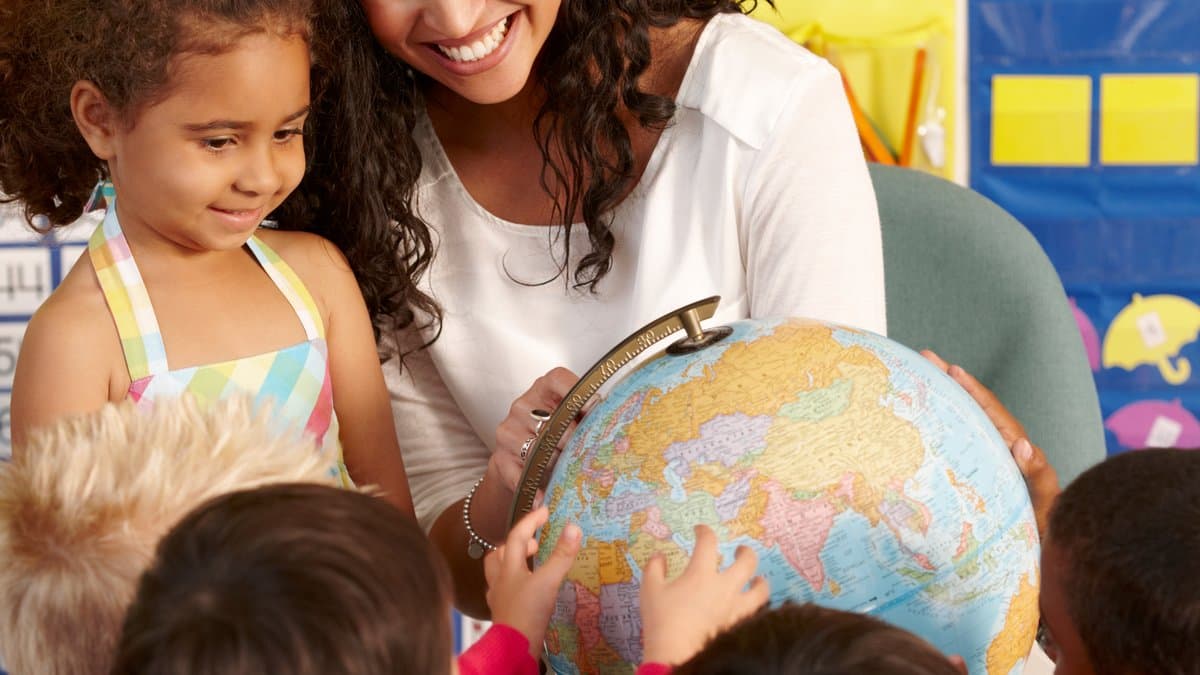 Niños aprendiendo con un globo terráqueo junto a su profesora